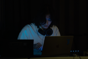 Junson Park in dark setting, lit by laptop screen and wearing headphones around neck