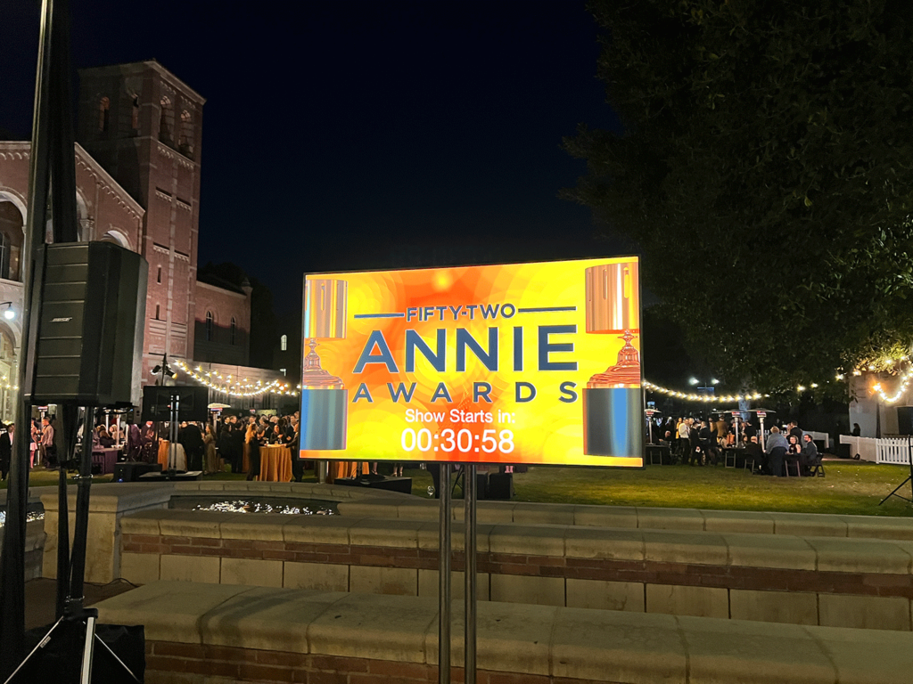 Large screen with Annie Awards logo and countdown clock propped up in courtyard at night