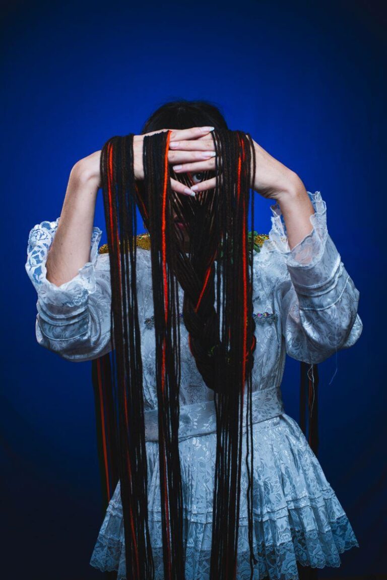 Anais Azul holds up long strands of hair in front of face, which is also obstructed by a braid