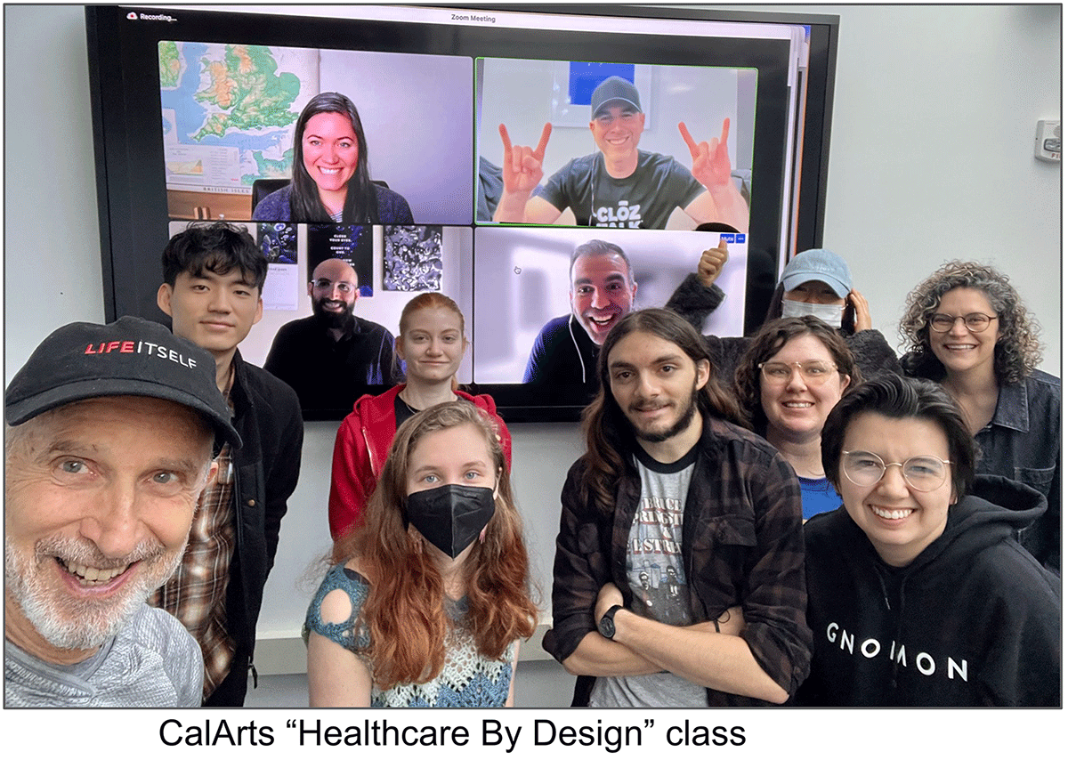 Two teachers and their students in a classroom smile in front of a screen with four people on Zoom