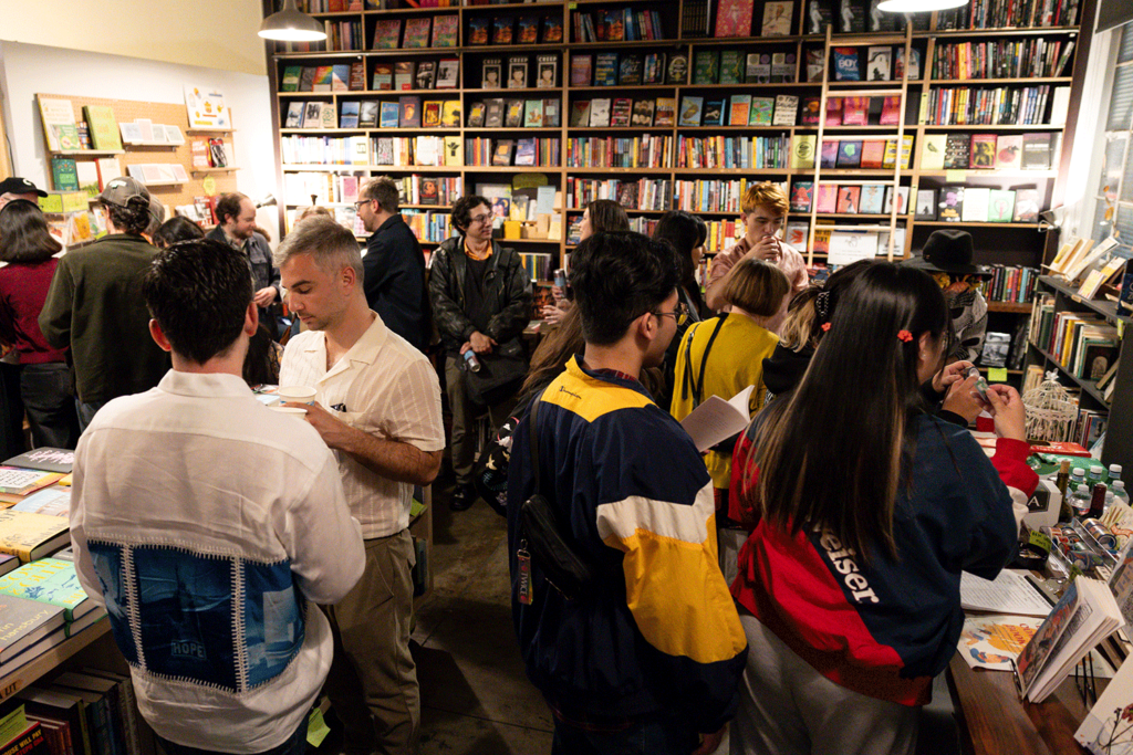 Bookshop filled with people chatting and browsing books, with shelves full of colorful titles in the background.