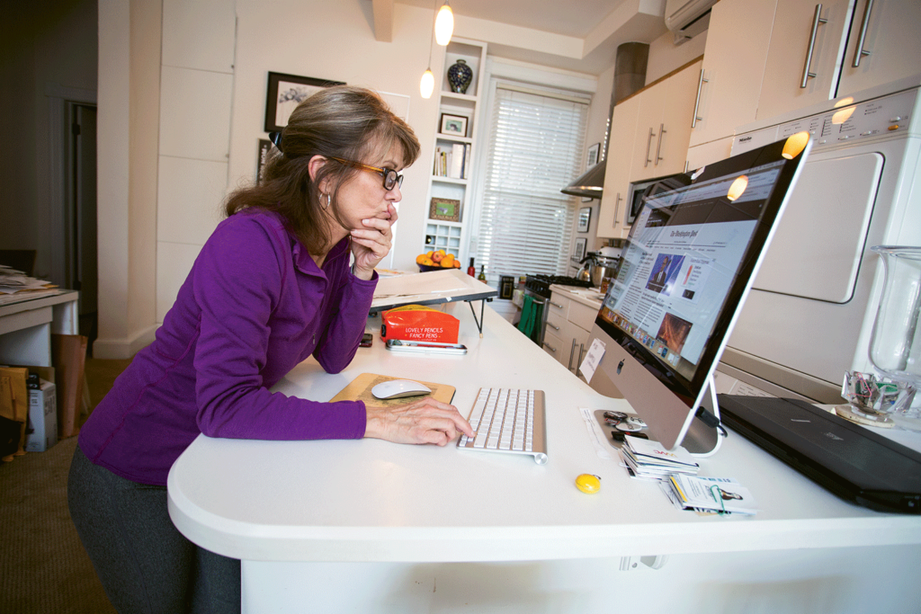 Ann Telnaes reading digital news on a monitor