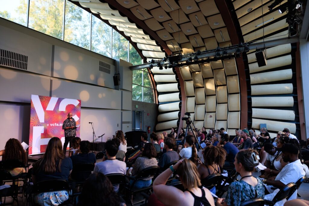 A man is onstage at a reading in front of a seated crowd.