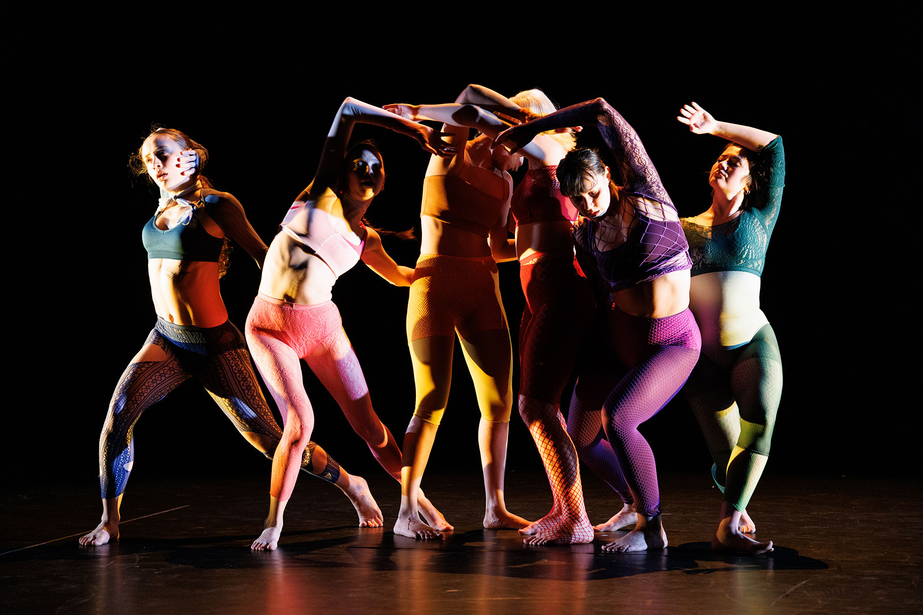 a group of dancers wearing colorful clothing and intertwined on a dark stage