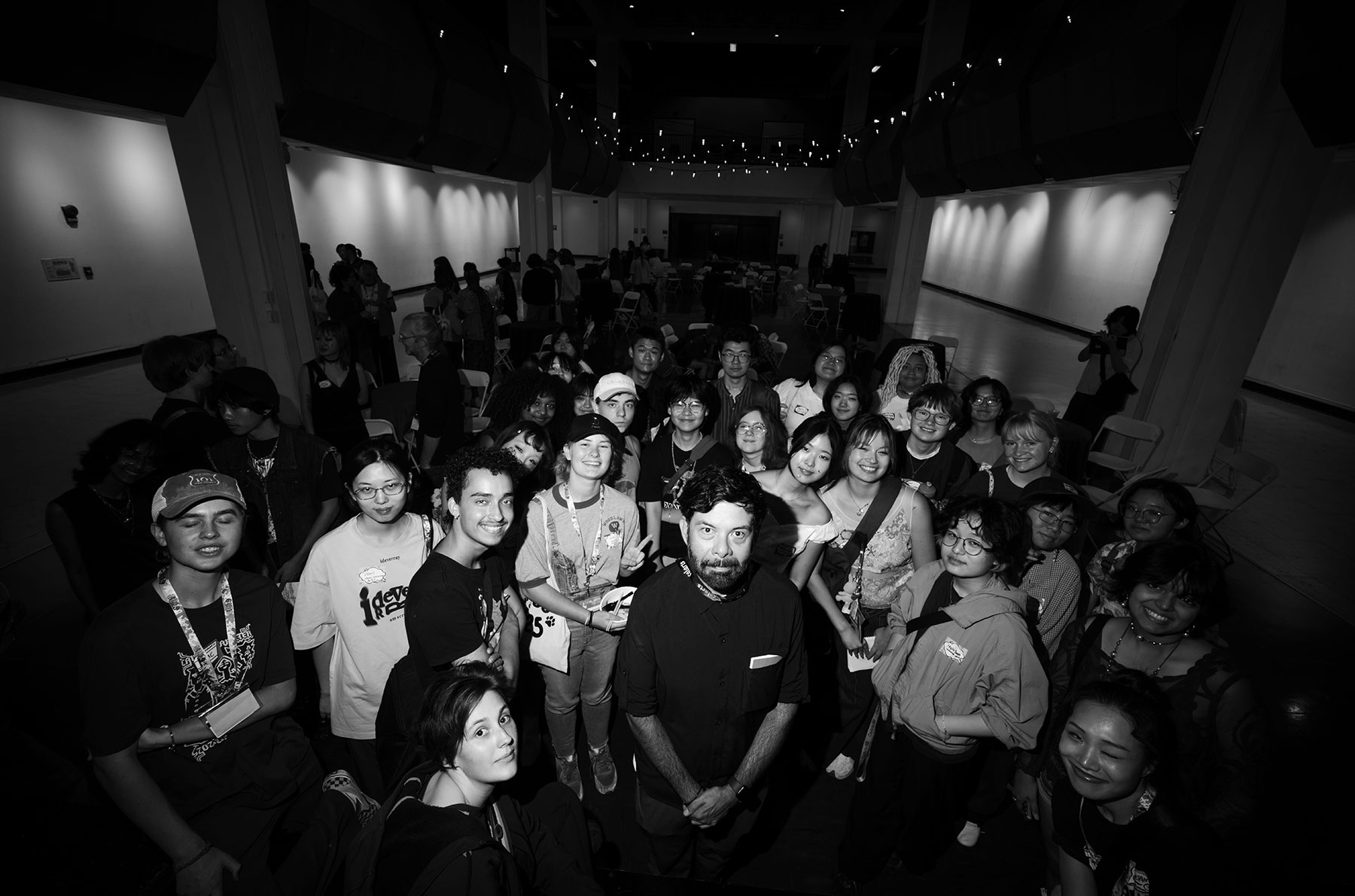 a black and white photo show a group of young adults gathered together in a large gallery space