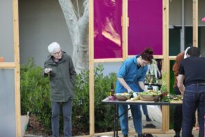 A woman with a glass of wine observes and art piece of making salad.