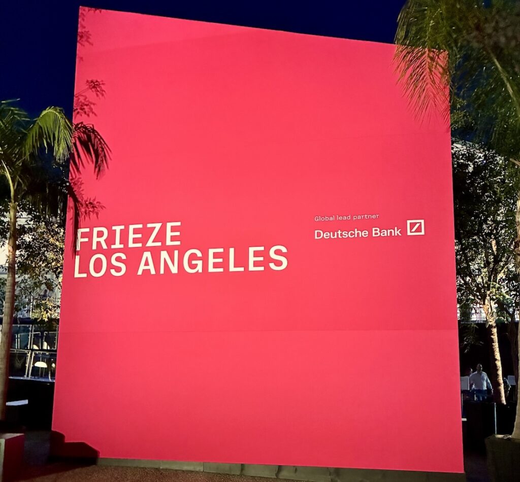 A large pink sign stands as tall as the palm trees that reads Frieze Los Angeles / Global Lead Sponsor Deutsche Bank