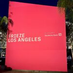 A large pink sign stands as tall as the palm trees that reads Frieze Los Angeles / Global Lead Sponsor Deutsche Bank