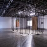 Gallery installation with hanging black sheer fabrics and rectangular painted canvases.