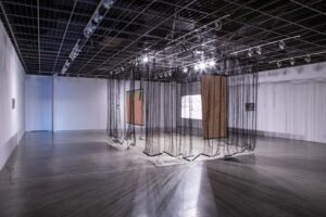 Gallery installation with hanging black sheer fabrics and rectangular painted canvases.