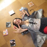 Person lying on a floor with headphones on, surrounded by CD cases.