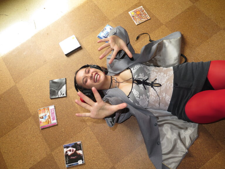 Person lying on a floor with headphones on, surrounded by CD cases.