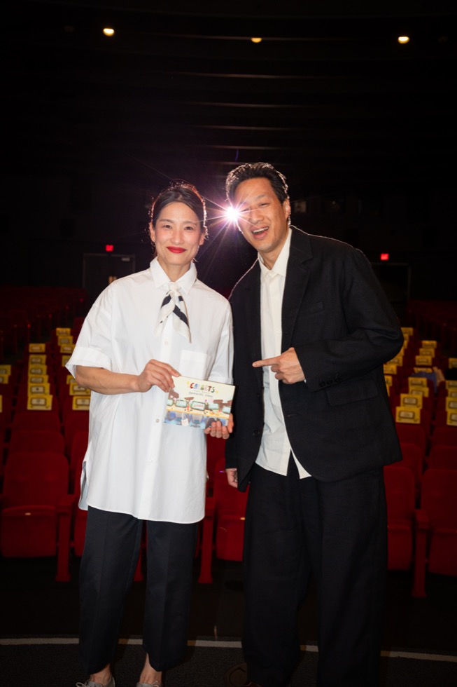 Two people stand in a dark theater holding up a program.
