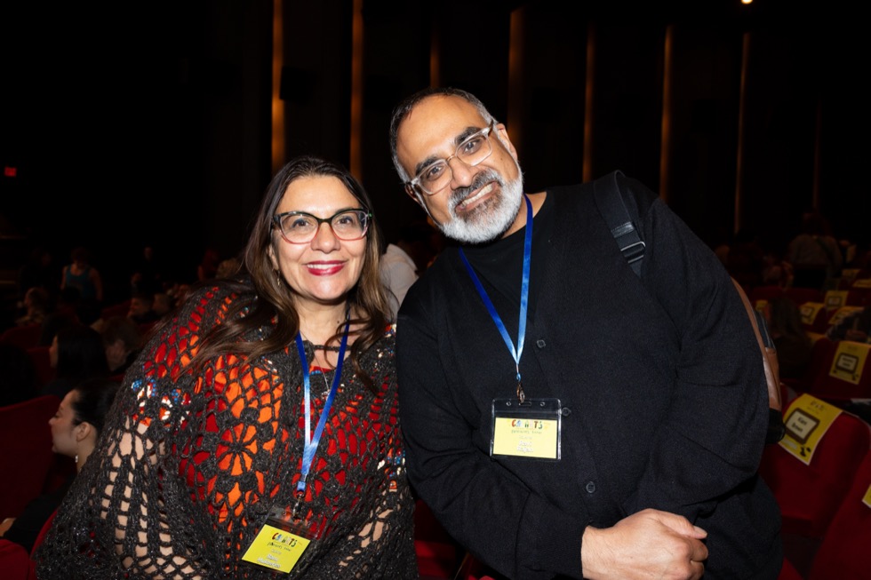 Two people wear name tags as they pose in a dark theater.