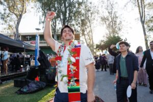 A CalArts grad in a white short-sleeve shirt raises his fist in the air while walking the graduation path.