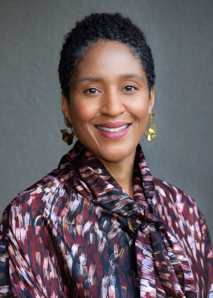 Headshot of a woman in a floral shirt and dangling earrings.