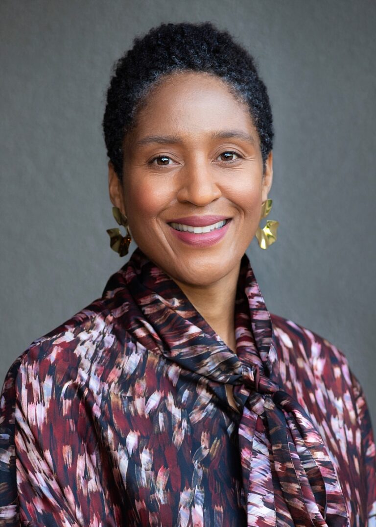 Headshot of a woman in a floral shirt and dangling earrings.