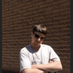 oliver tree in a t-shirt, shades, arms crossed against a brick wall.