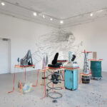 An art exhibition installation featuring various sculptures on pedestals, a whimsical mural on the wall, and colorful confetti on the floor.