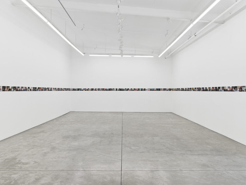 A white gallery is lined by small photos in a straight line around the walls.