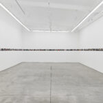 A white gallery is lined by small photos in a straight line around the walls.