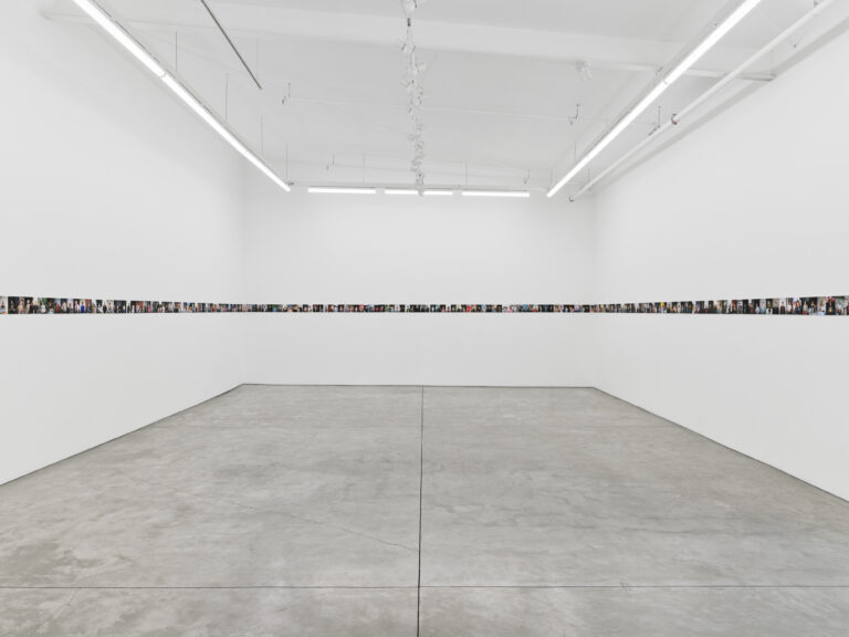 A white gallery is lined by small photos in a straight line around the walls.
