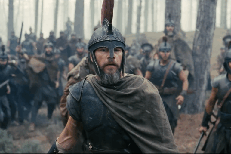 Matt Damon as Odysseus, wearing armor and standing among soldiers in a forest in The Odyssey.