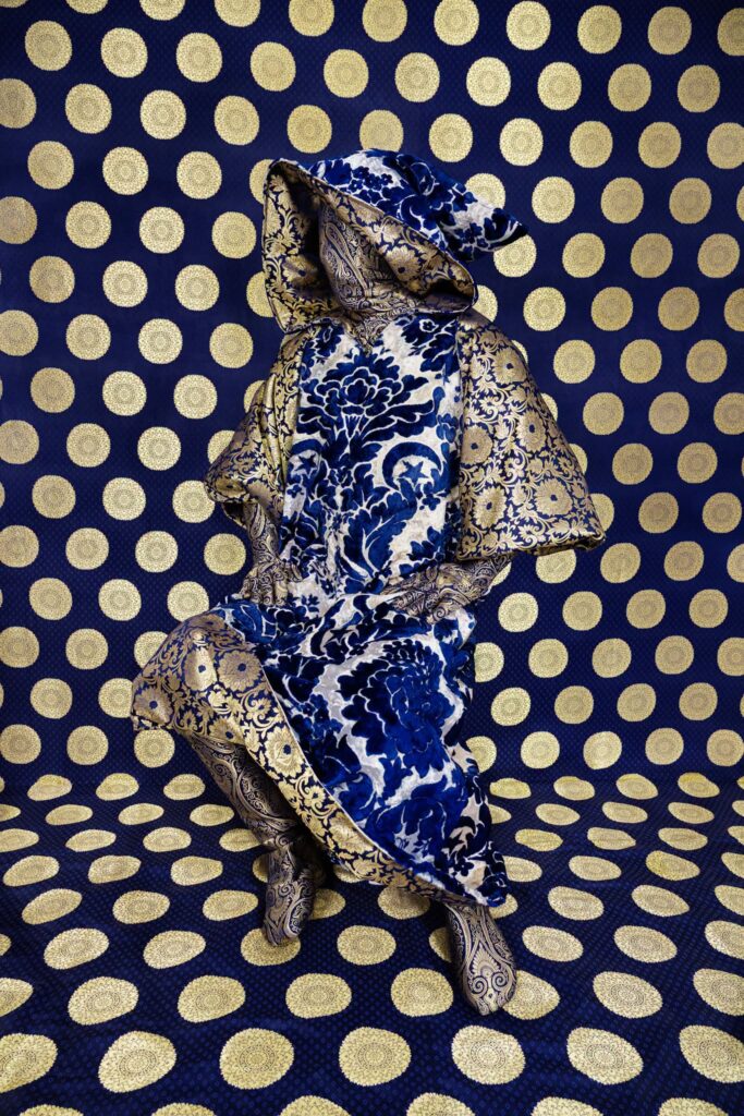 An art piece where a mannequin in covered in fabric against a bright wall also covered in fabric.