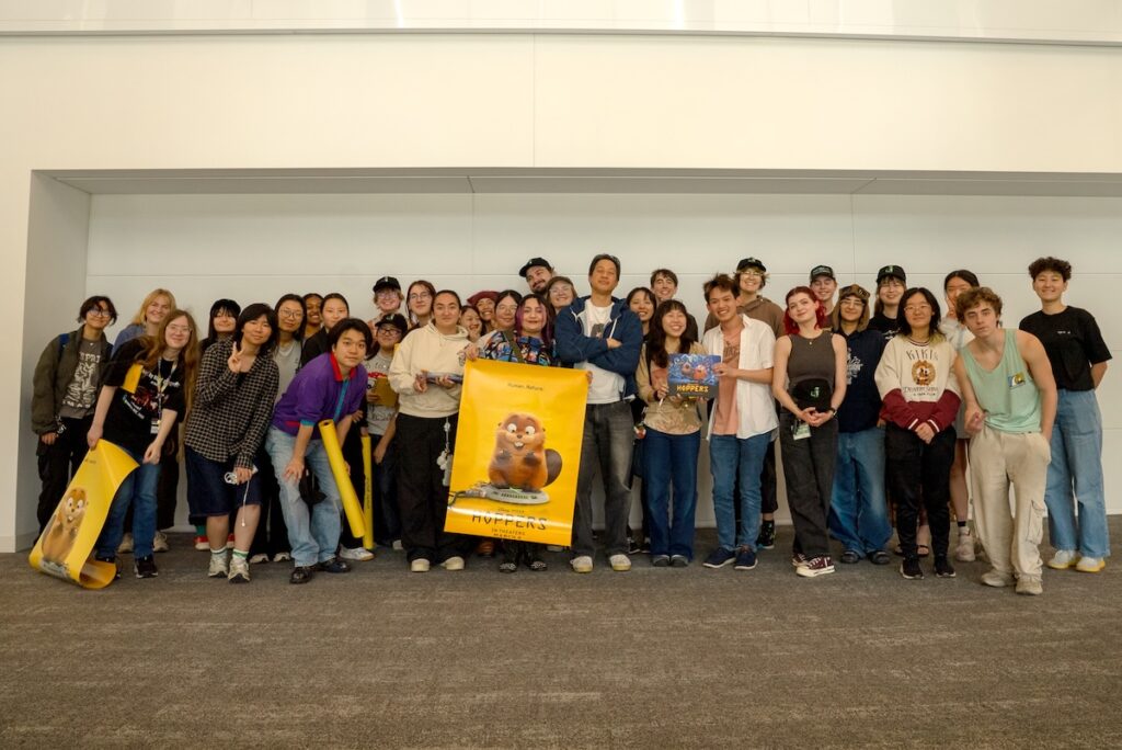 Filmmaker Daniel Chong poses at the center with a group of CalArts students, some holding yellow posters featuring the main character of 'Hoppers.'