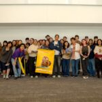 Filmmaker Daniel Chong poses at the center with a group of CalArts students, some holding yellow posters featuring the main character of 'Hoppers.'