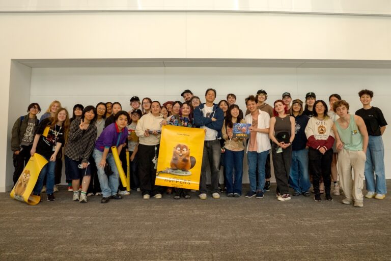 Filmmaker Daniel Chong poses at the center with a group of CalArts students, some holding yellow posters featuring the main character of 'Hoppers.'