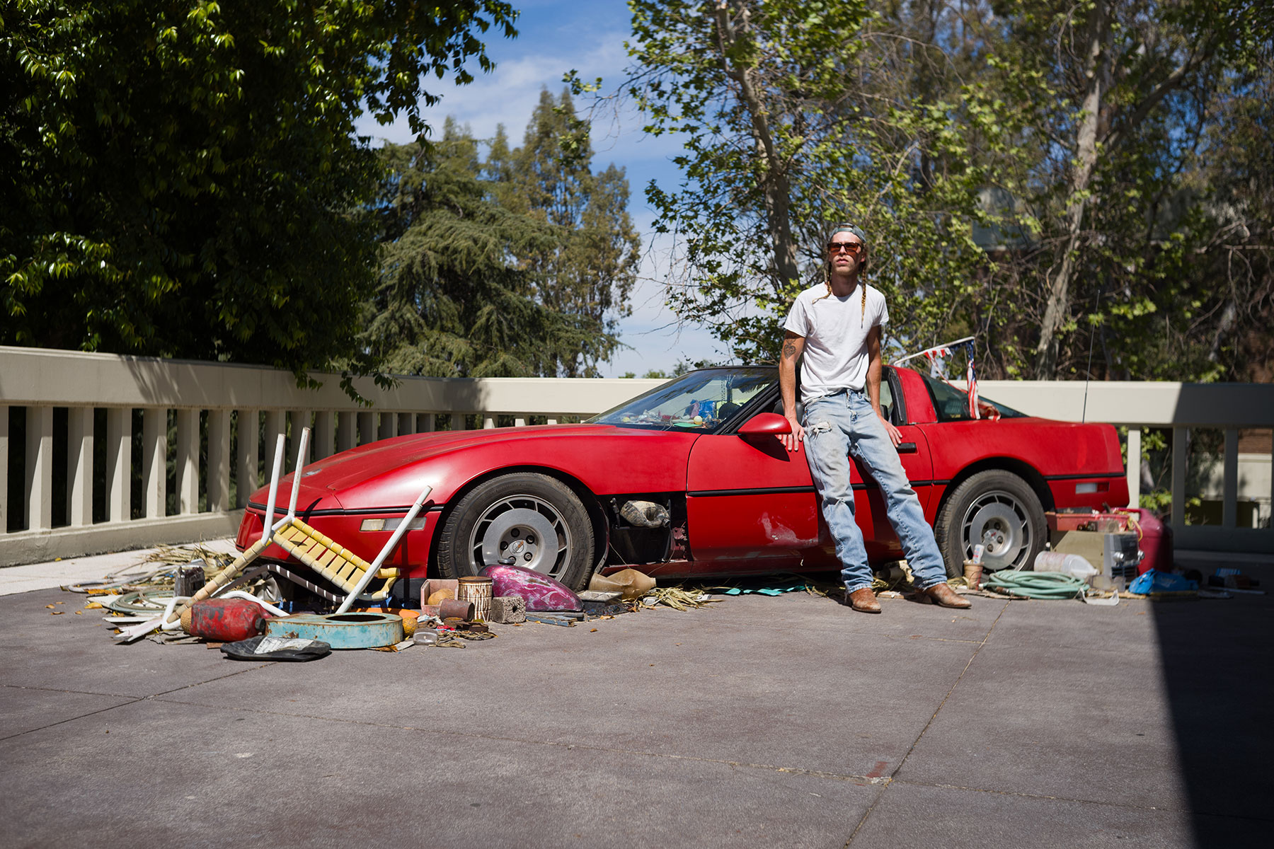 Man leaning against a red sports car with scattered items around.