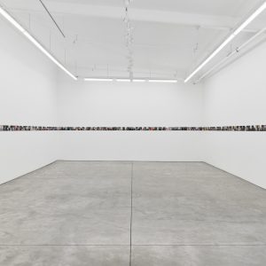 A white gallery is lined by small photos in a straight line around the walls.