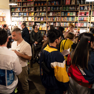 Bookshop filled with people chatting and browsing books, with shelves full of colorful titles in the background.