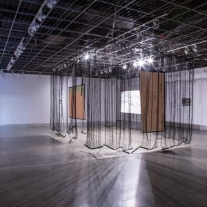 Gallery installation with hanging black sheer fabrics and rectangular painted canvases.