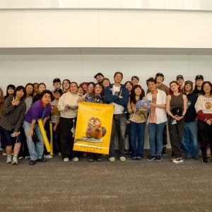 Filmmaker Daniel Chong poses at the center with a group of CalArts students, some holding yellow posters featuring the main character of 'Hoppers.'