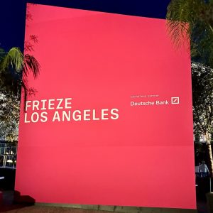 A large pink sign stands as tall as the palm trees that reads Frieze Los Angeles / Global Lead Sponsor Deutsche Bank