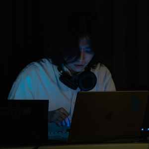 Junson Park in dark setting, lit by laptop screen and wearing headphones around neck