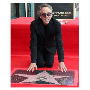 Tim Burton kneeling on a red carpet as he touches his star on the Hollywood Walk of Fame.