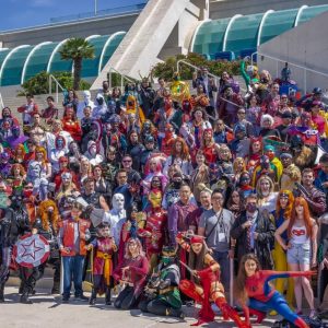 A diverse group of people dressed in various superhero costumes stands on steps outdoors, with modern architecture in the background.
