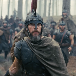 Matt Damon as Odysseus, wearing armor and standing among soldiers in a forest in The Odyssey.